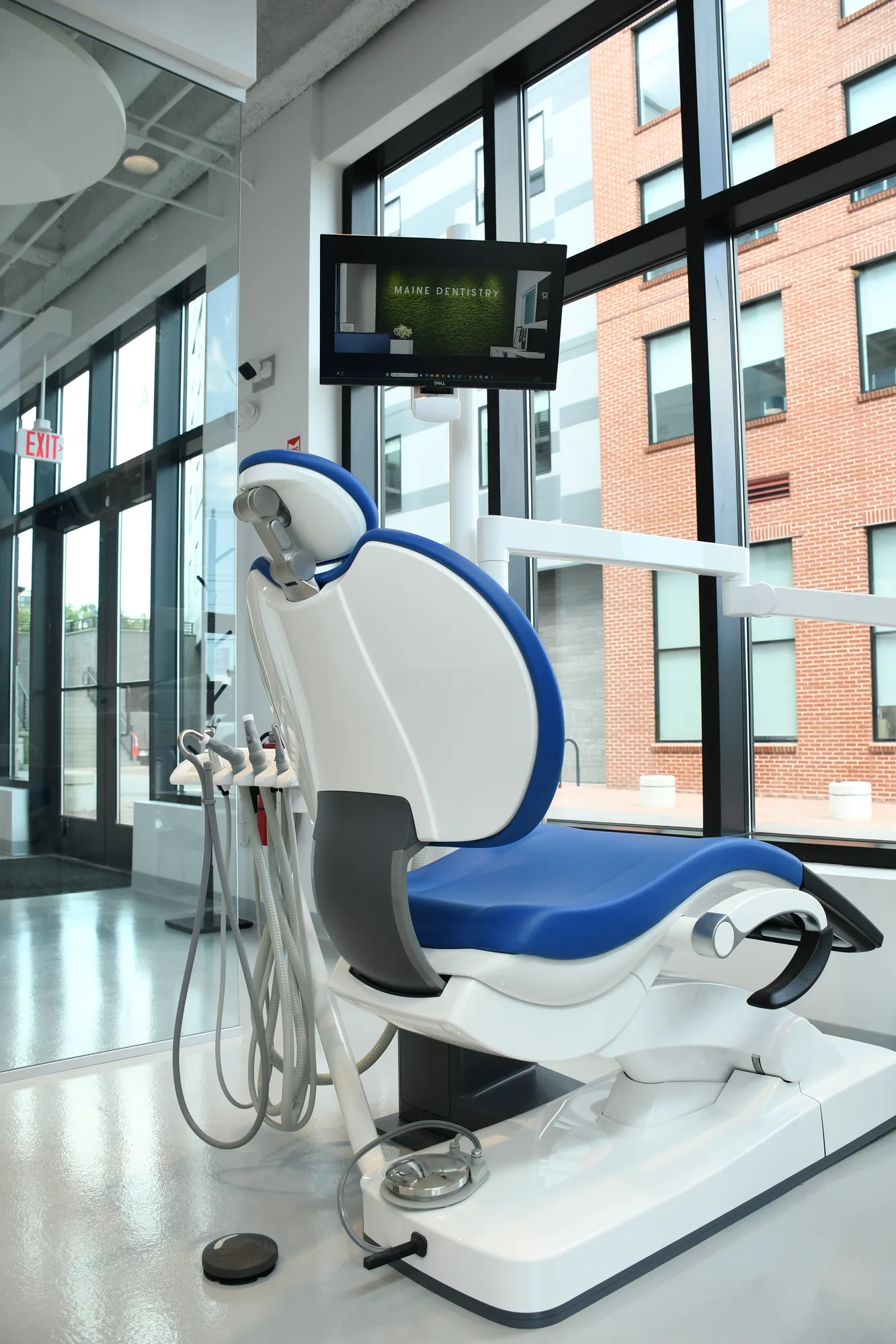 A sunlit Maine Dentistry treatment room with tall windows and a blue dental chair