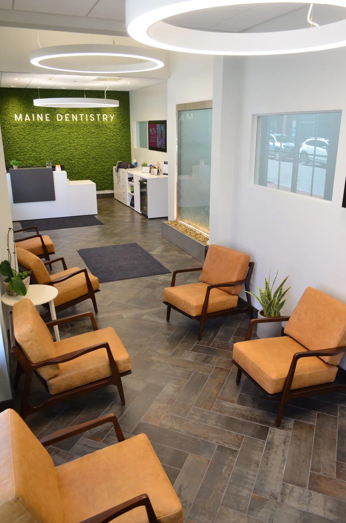 Maine Dentistry reception and seating area with tan chairs and a green wall behind the front desk